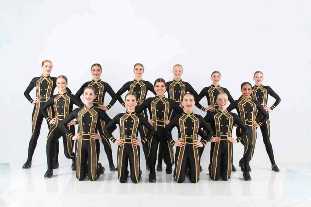 group of teenage tap dancers in black and gold costumes